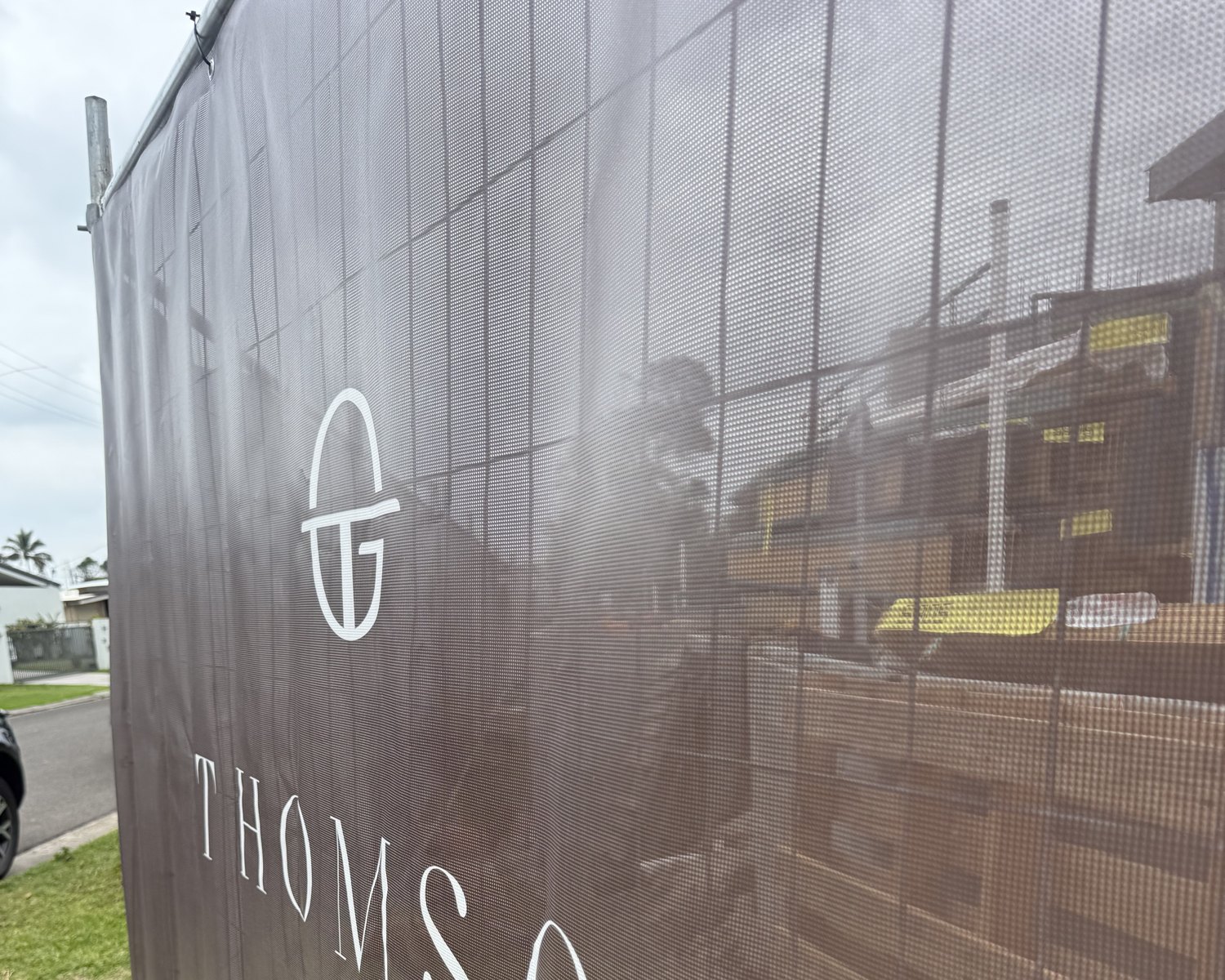 Close-up of printed PVC mesh banner showing the logo, metal eyelets and cable-tie fixings to the fence panel