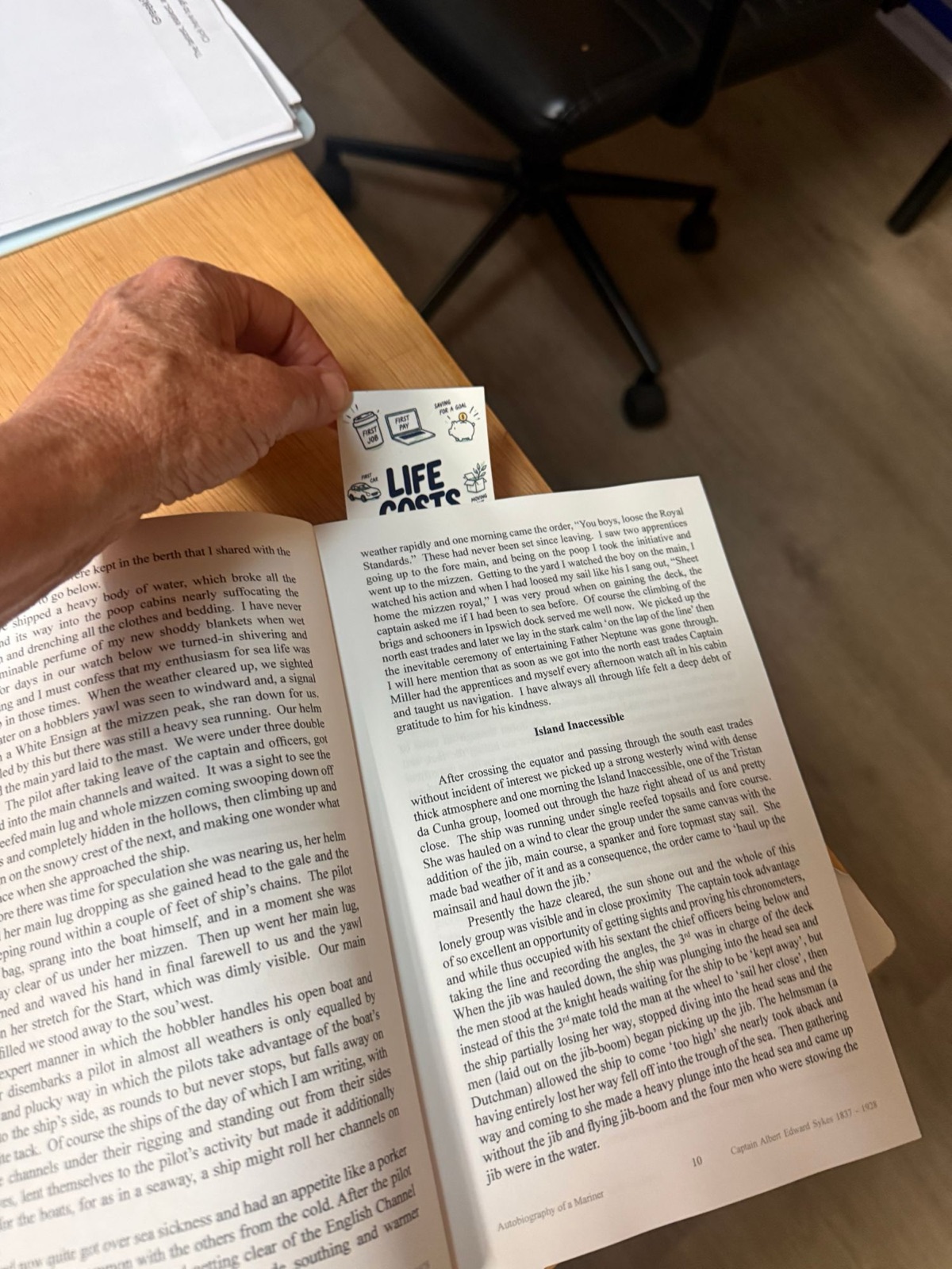 Hand lifting the Life Costs Money bookmark out of an open book on a desk