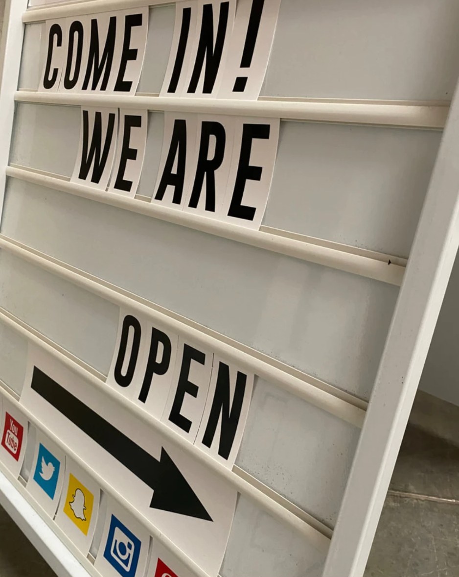 White letterboard-style A-frame sign with changeable black letters reading Come in! We are open