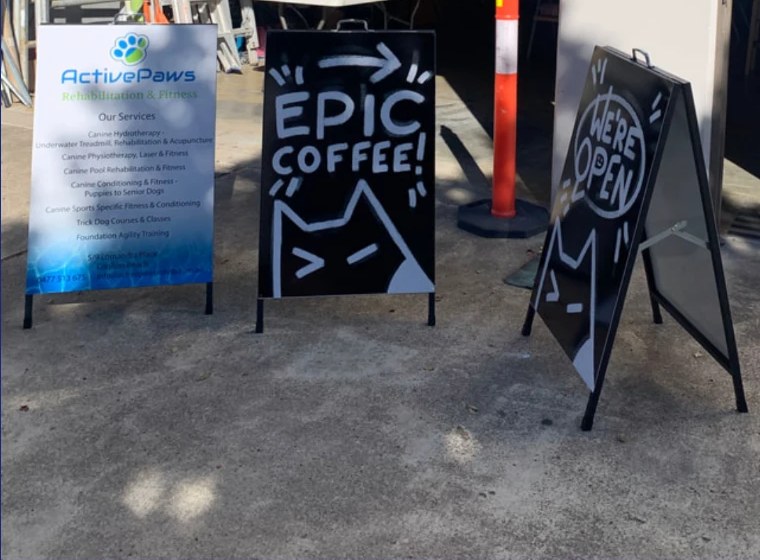 Three A-frame signs — a printed panel sign, a hand-painted black board and a black open board — outside the Sykes Signs workshop