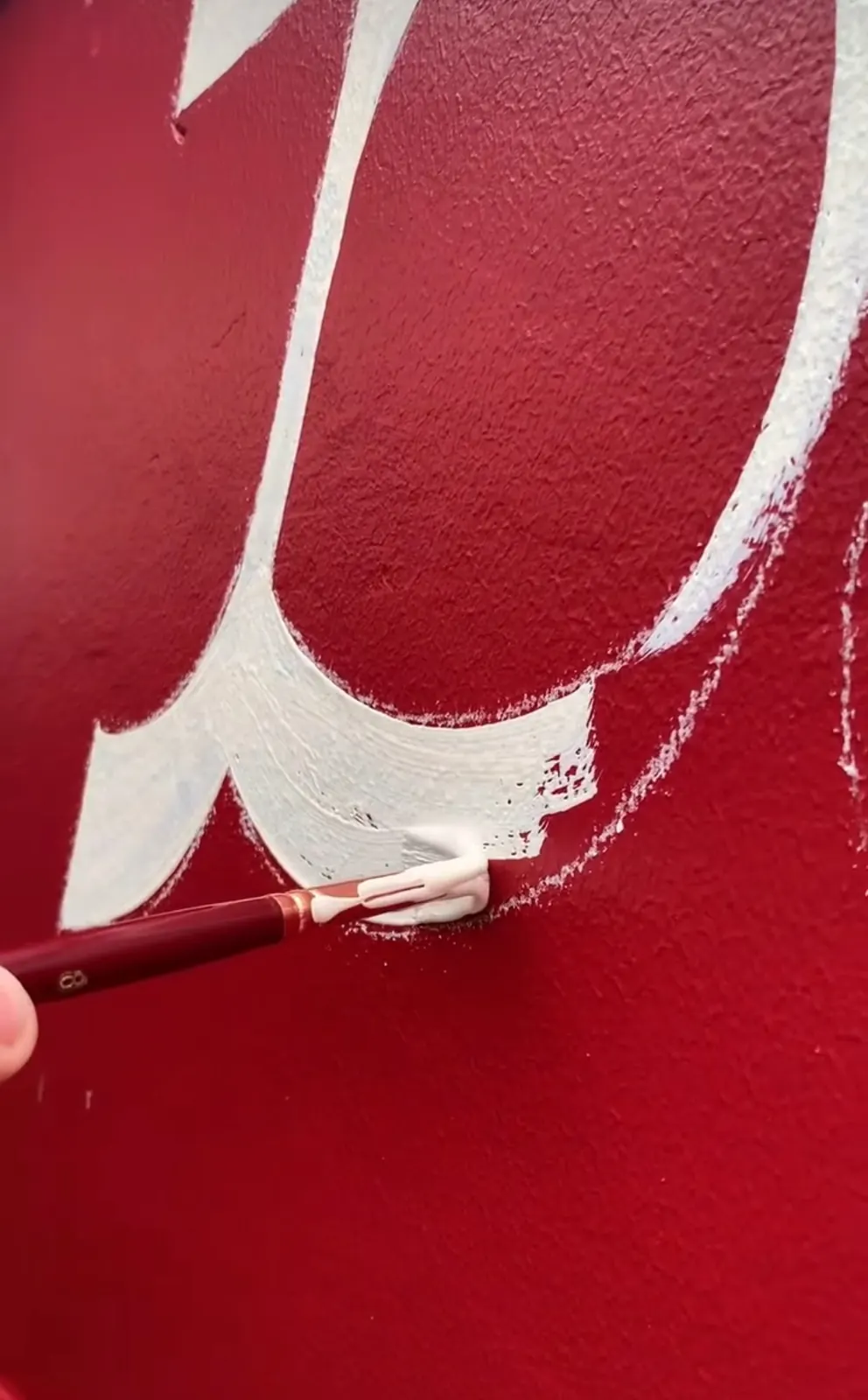 Hand sign-writing brush painted lettering on a red wall by Sykes Signs